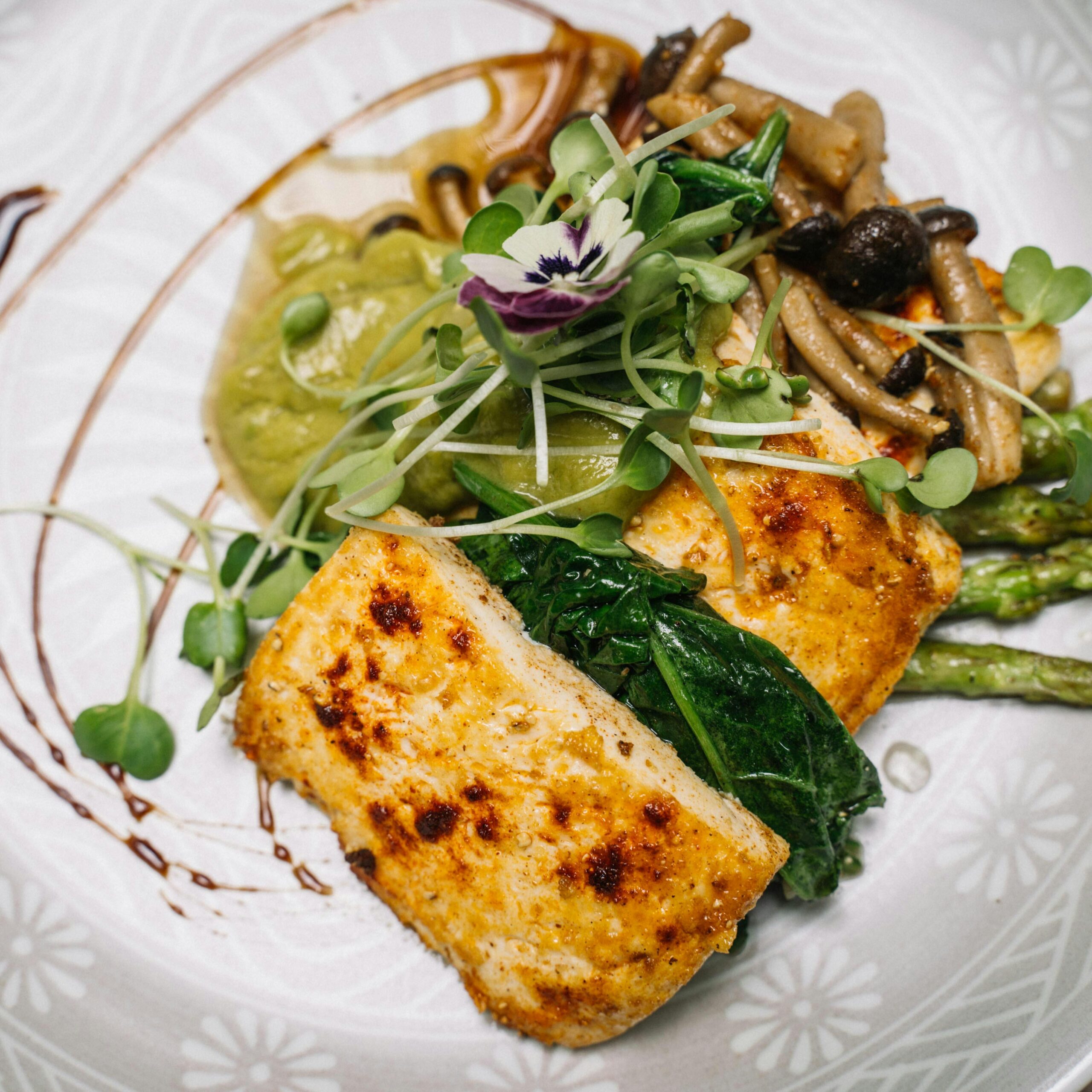 Deliciously plated tofu with asparagus, mushrooms, and edible flower garnish.