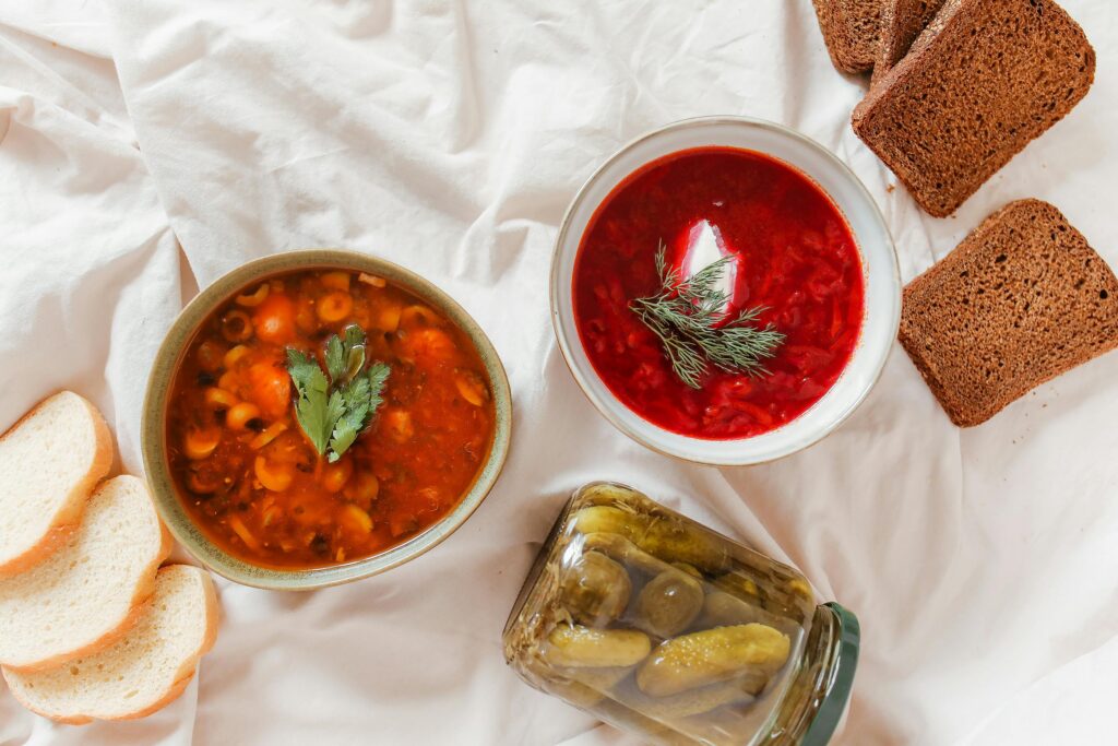 Overhead shot of traditional Russian dishes borscht, solyanka, and rye bread accompanied by pickles.